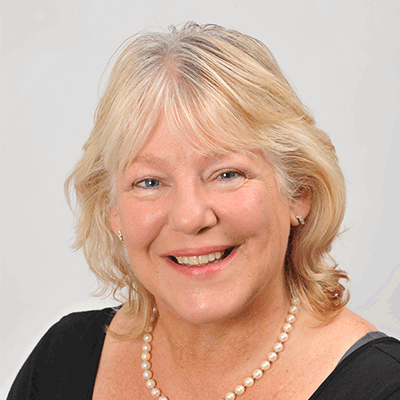 A head and shoulders shot of a smiling Hilary Mullen looking directly into the camera stood against a grey background